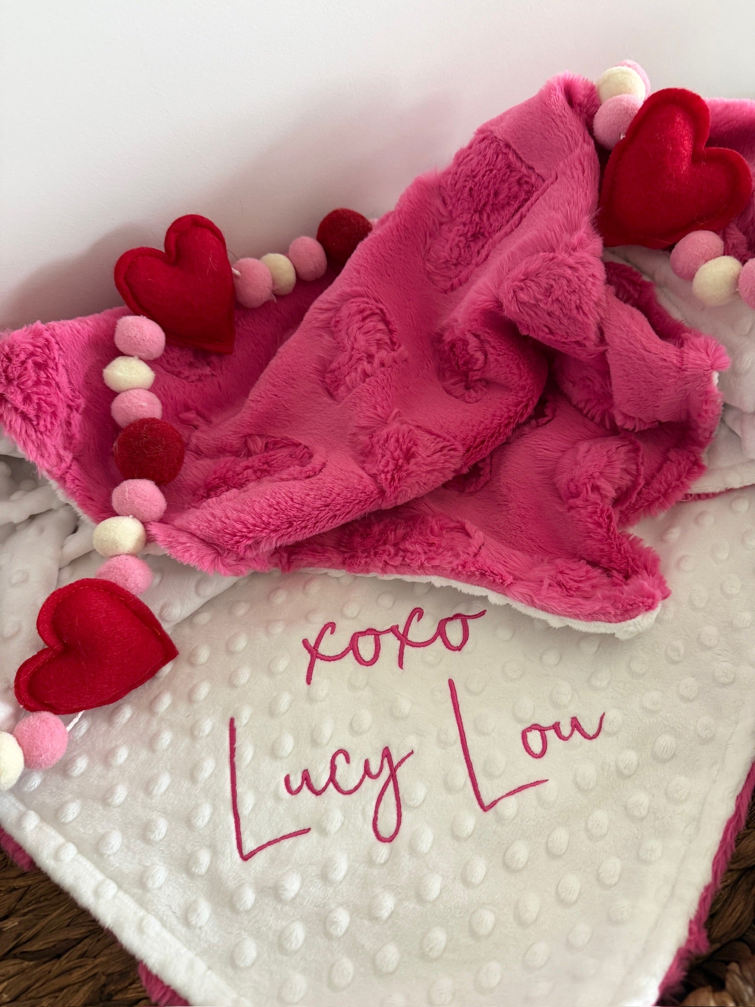 Pink and white blanket with 'xoxo Lucy Lou' text, surrounded by heart-shaped decorations.