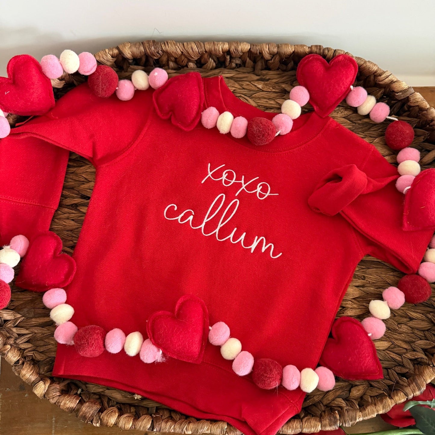 Red sweatshirt with 'Xoxo Callum' text on a decorative tray with heart and pom-pom decorations.