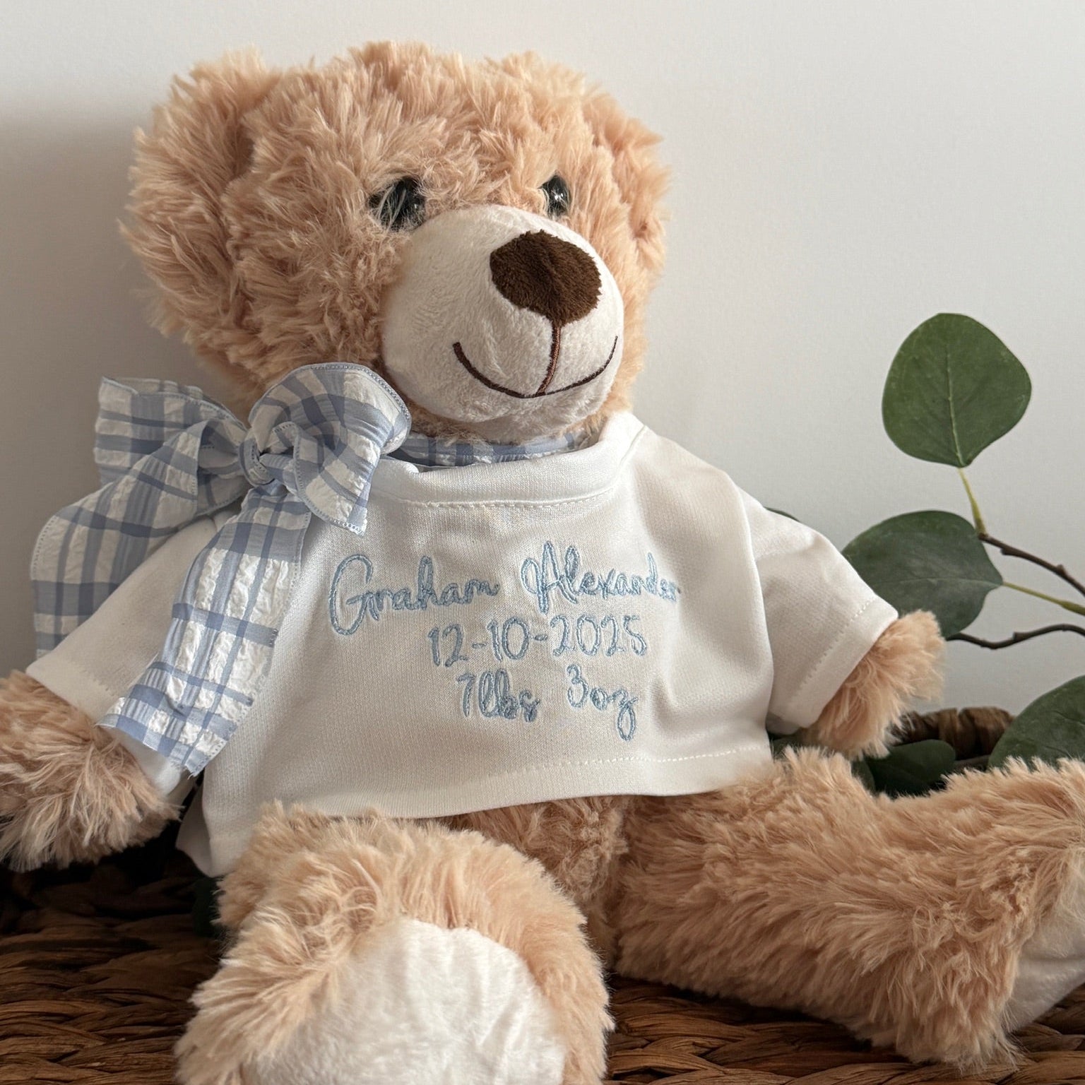 Teddy bear wearing a white shirt with blue text, sitting on a woven surface.