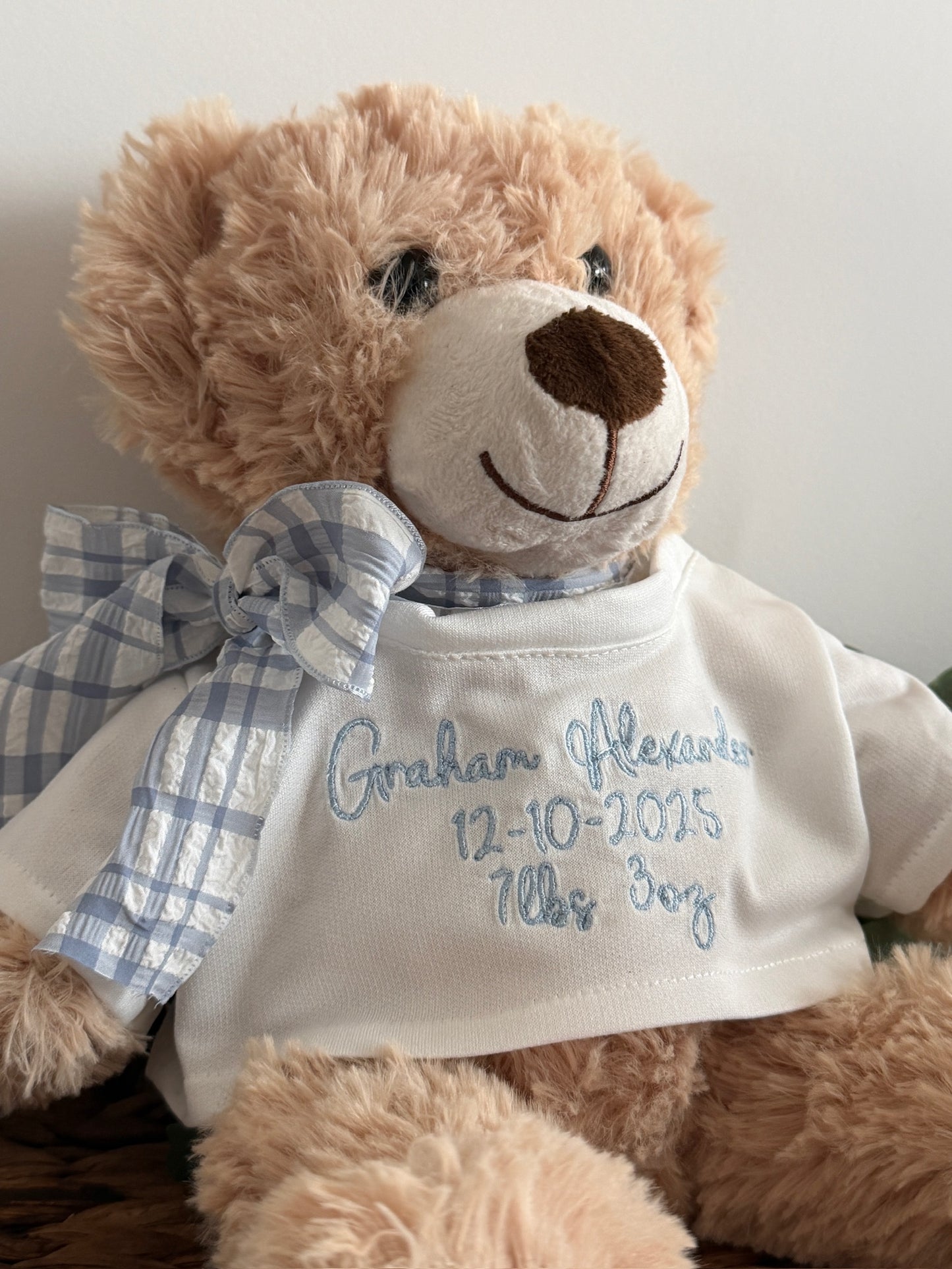 Teddy bear wearing a white shirt with embroidered text, sitting on a wooden surface.