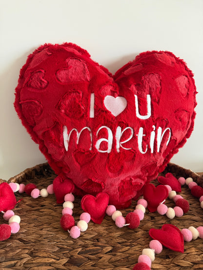 Red heart-shaped pillow with 'I  ❤️ U  ❤️ Martin' text on a woven surface.