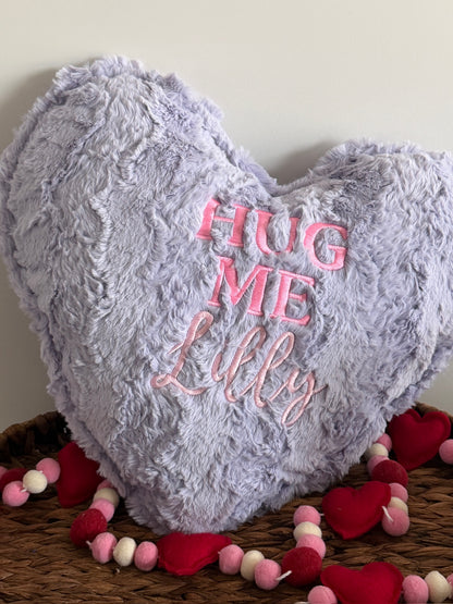 Heart-shaped pillow with 'HUG ME Lilly' text on a wooden surface with decorative hearts and beads.