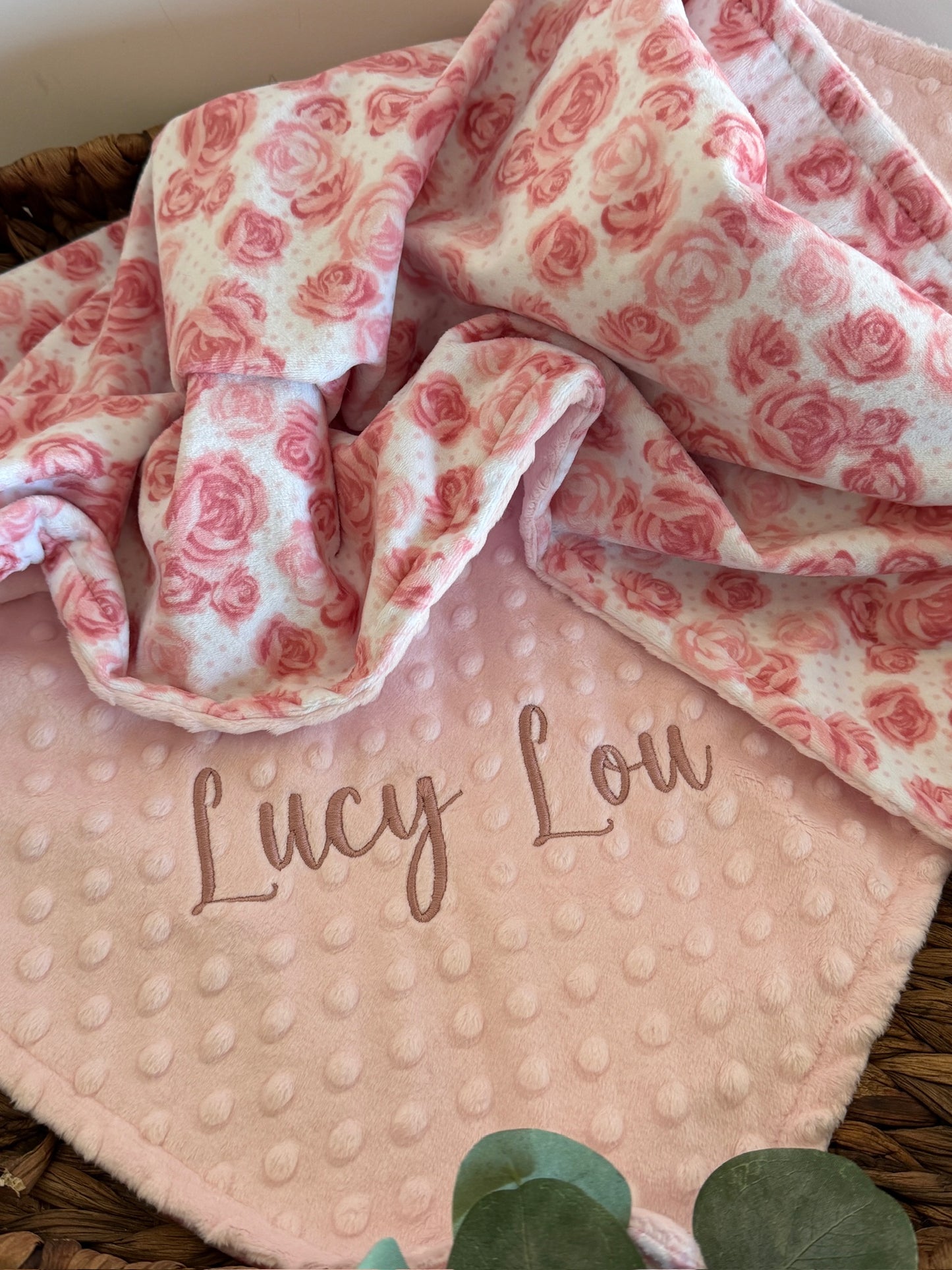 Floral patterned blanket with 'Lucy Lou' embroidery on a pink textured fabric background.