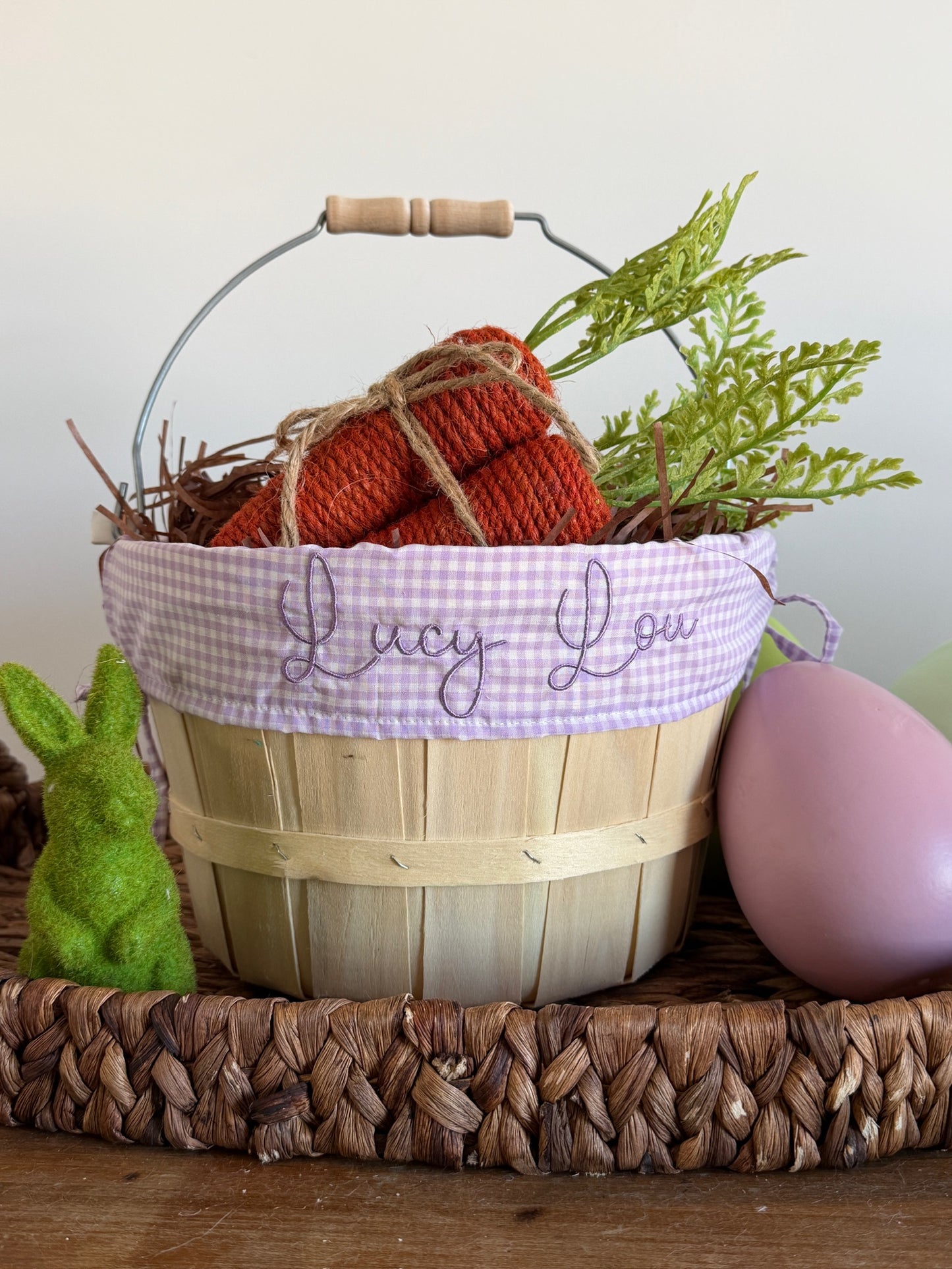 Wooden Easter basket with knitted carrots, greenery, and a pink egg on a wooden surface.