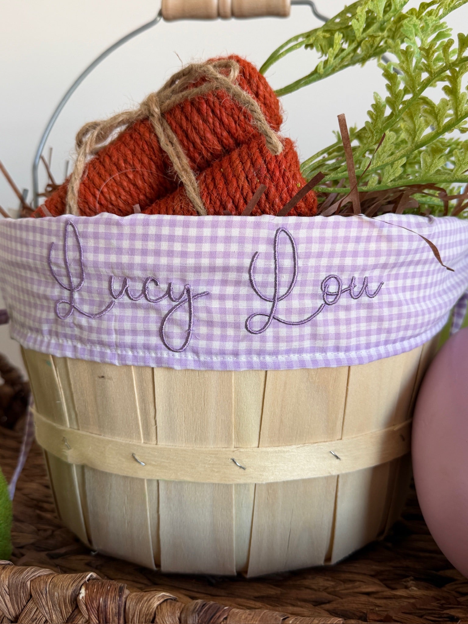 Wooden basket with a purple gingham lid featuring 'Lucy Lou', filled with red yarn balls.