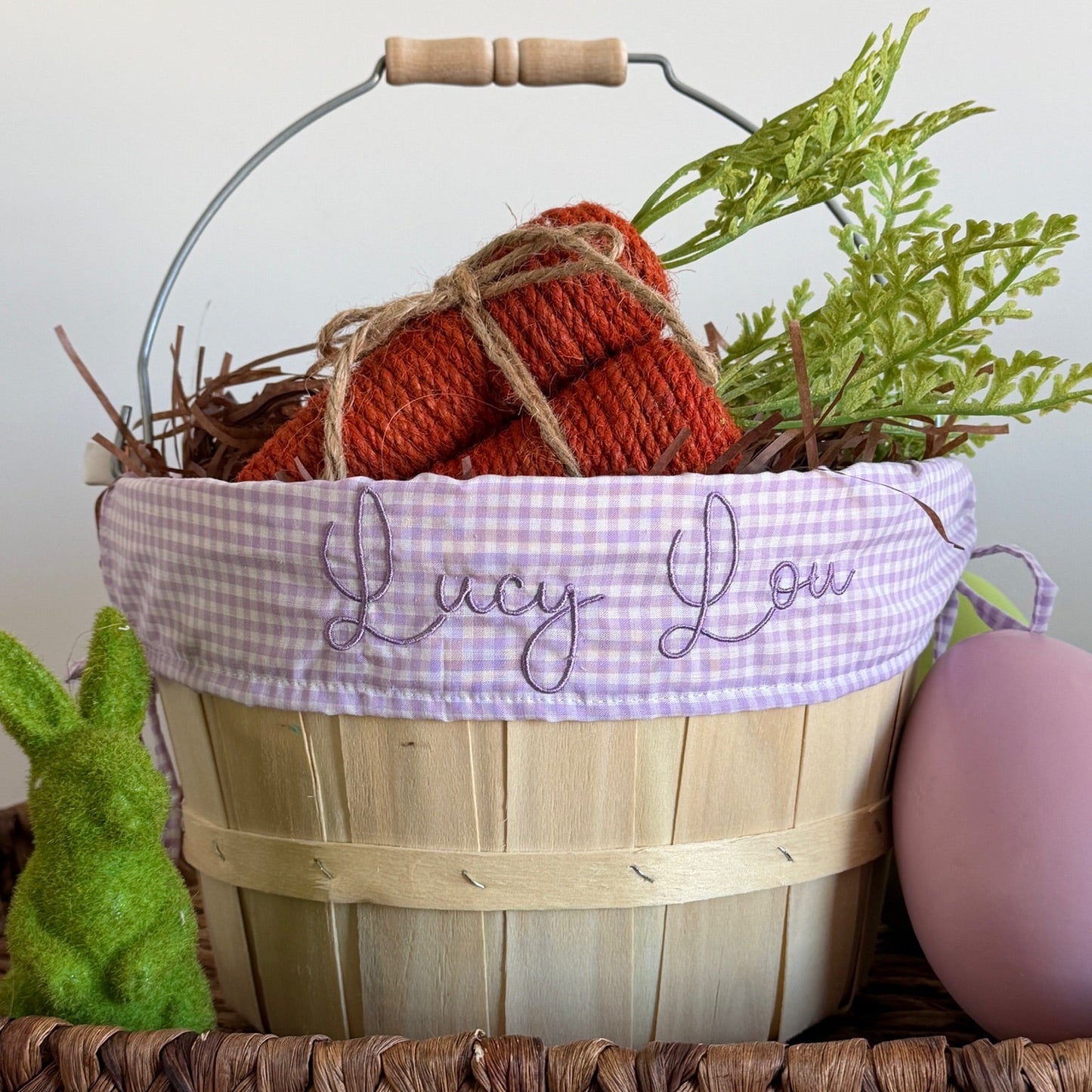 Basket with knitted items and greenery, featuring 'Lucy Lou' branding, on a wooden surface.