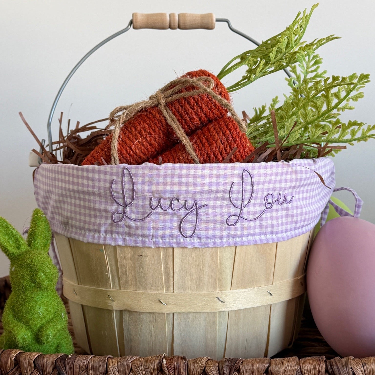 Basket with knitted items and greenery, featuring 'Lucy Lou' branding, on a wooden surface.