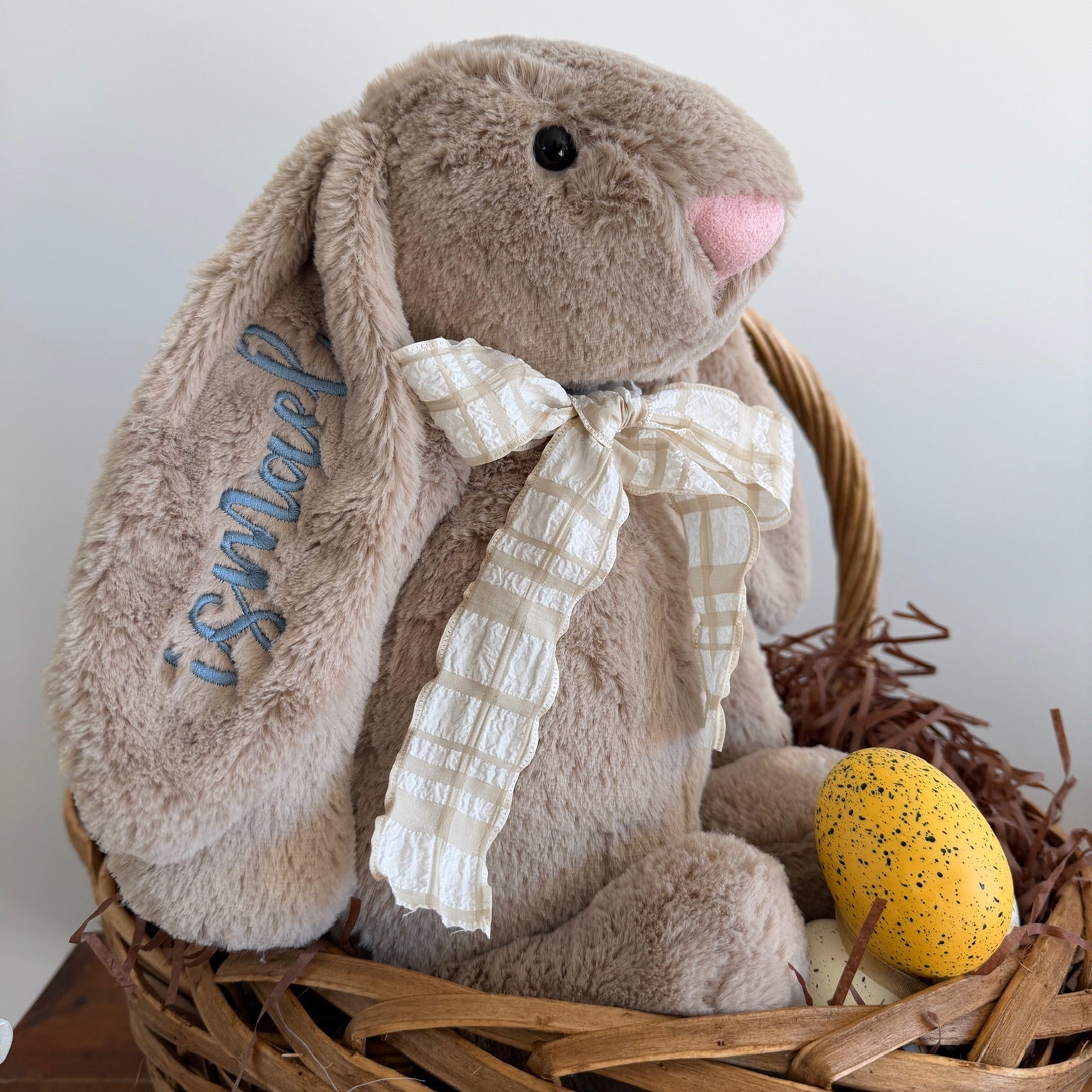 Plush bunny with a bow in a wooden basket with a yellow egg on a white background