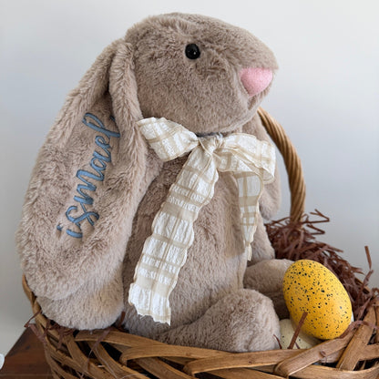 Plush bunny with a bow in a wooden basket with a yellow egg on a white background