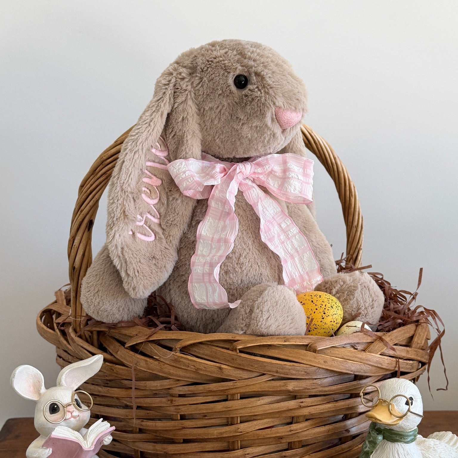 Stuffed bunny with a pink bow in a wicker basket on a wooden surface.
