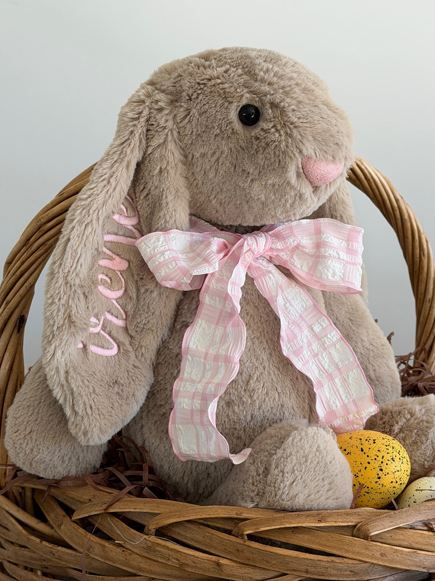 Plush bunny with a pink bow in a wicker basket on a light background