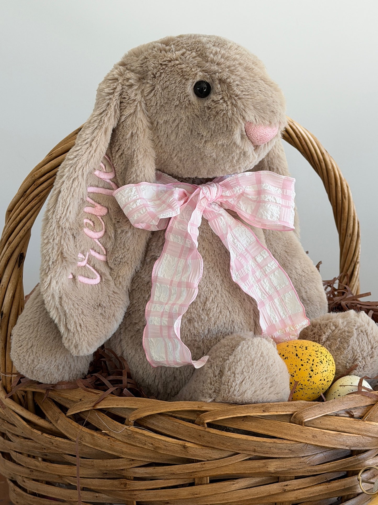 Stuffed bunny with a pink bow in a wicker basket on a light background
