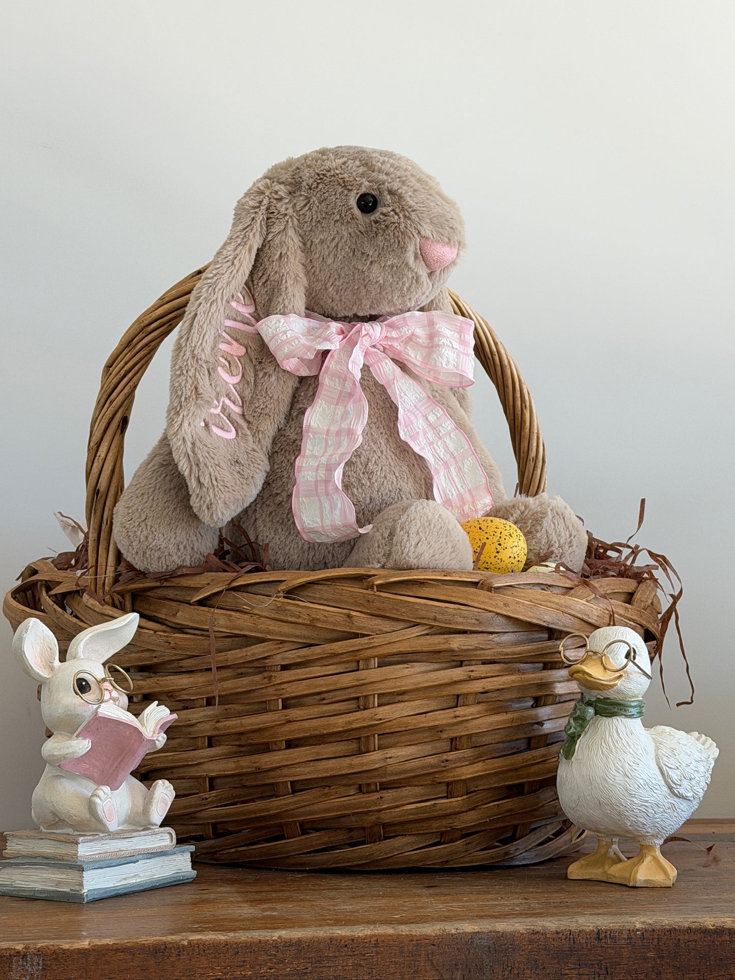 Decorative basket with plush bunny, duck, and small rabbit figure on a wooden surface.