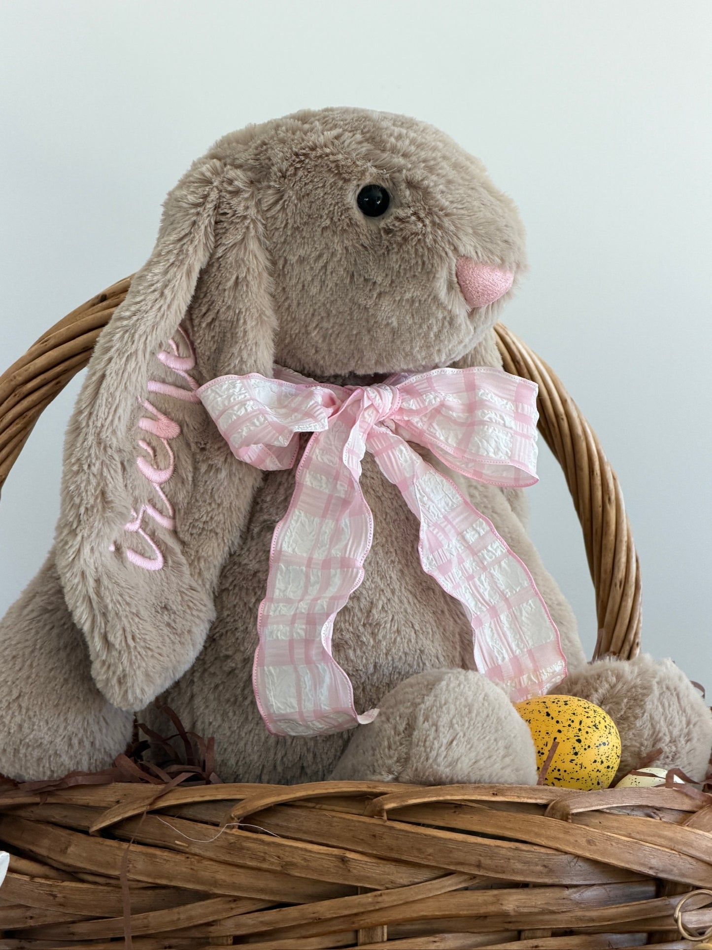 Stuffed bunny with a pink bow in a wicker basket on a light background