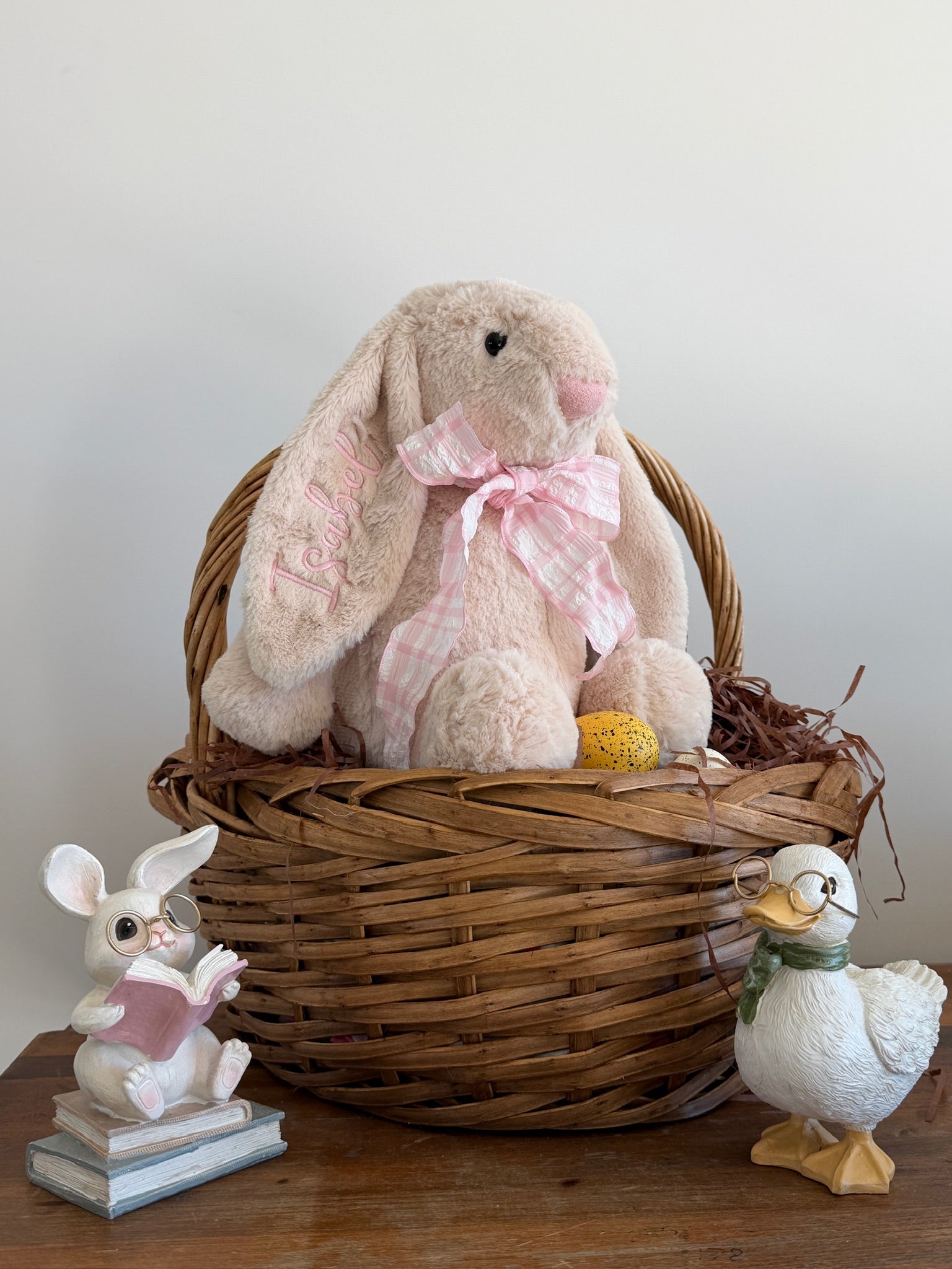 Wicker basket with plush bunny, small rabbit figurine, and duck on a wooden surface.