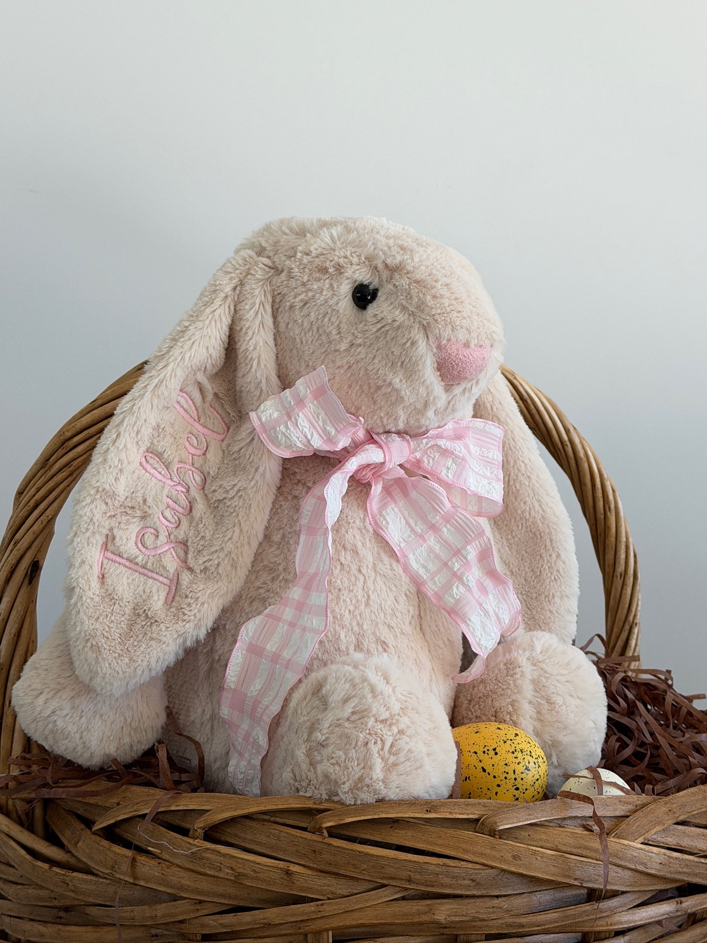 Stuffed bunny with a pink bow in a wicker basket on a light gray background