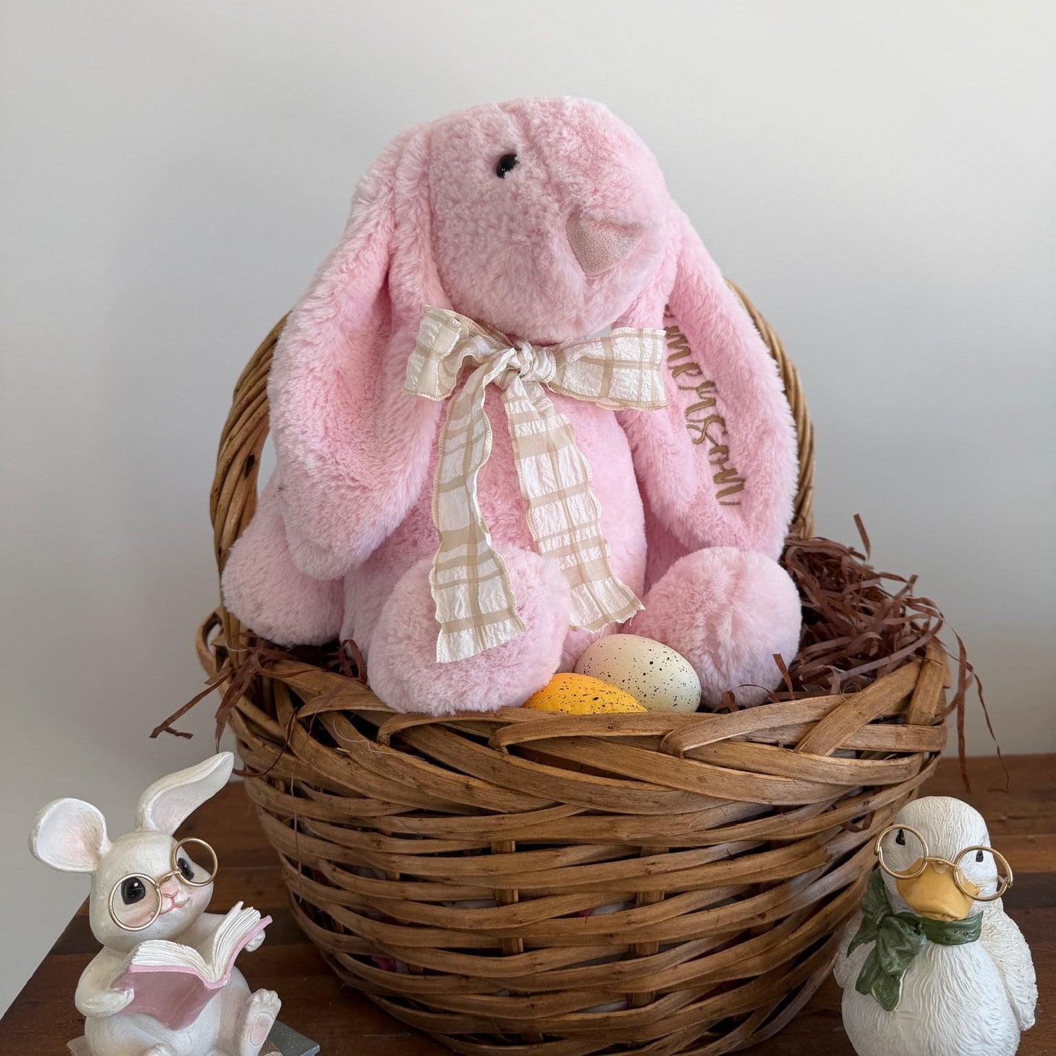 Pink plush bunny in a wicker basket with decorative elements on a wooden surface.