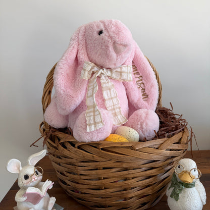 Pink plush bunny in a wicker basket with decorative elements on a wooden surface.