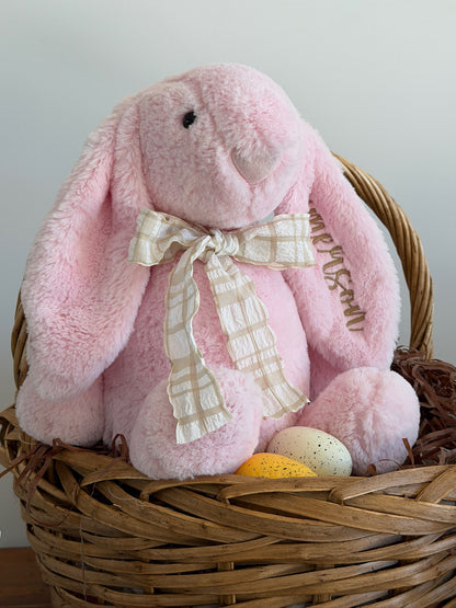 Pink plush bunny with a bow in a wicker basket on a light gray background