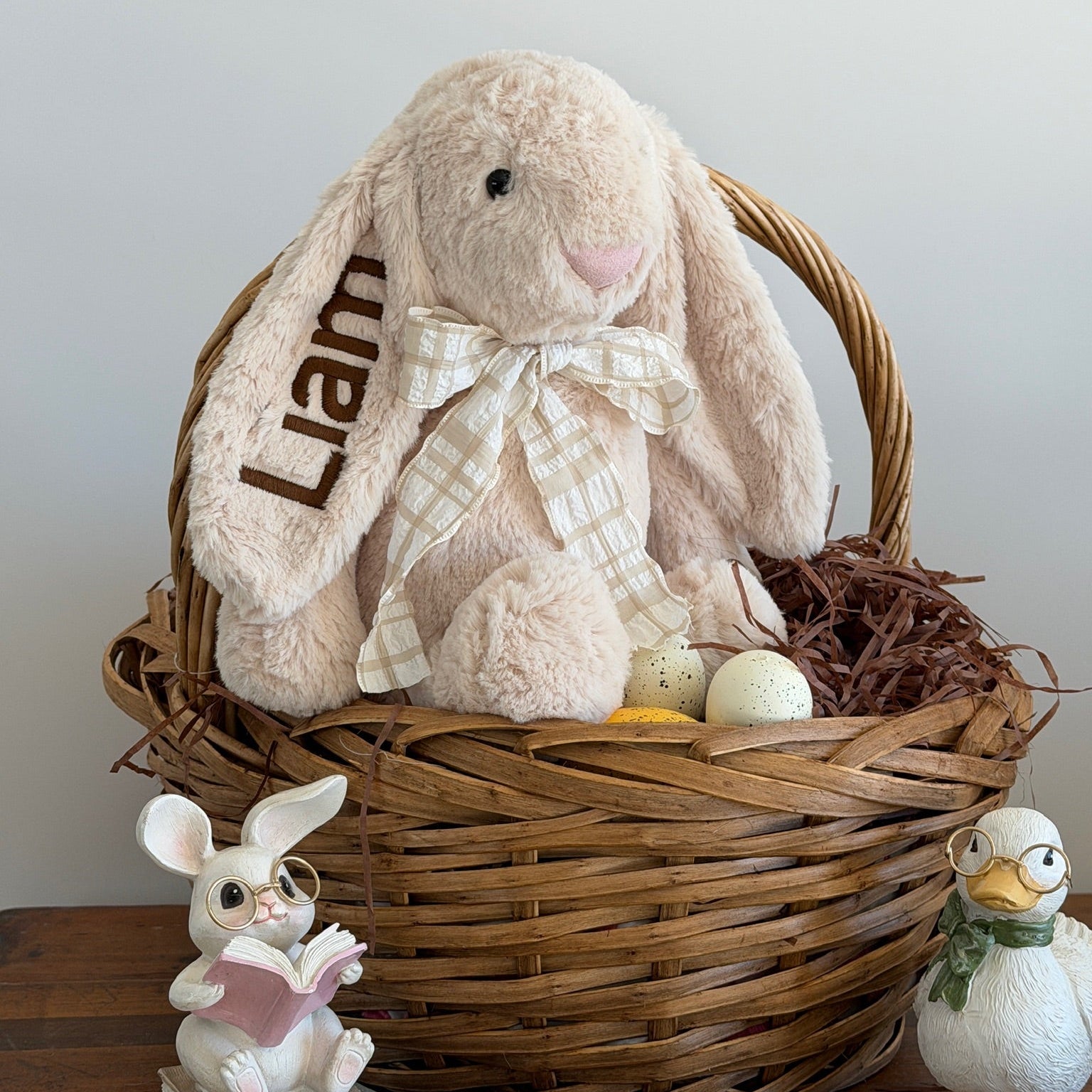 Wicker basket with plush bunny, decorative eggs, and small figurines on a wooden surface.
