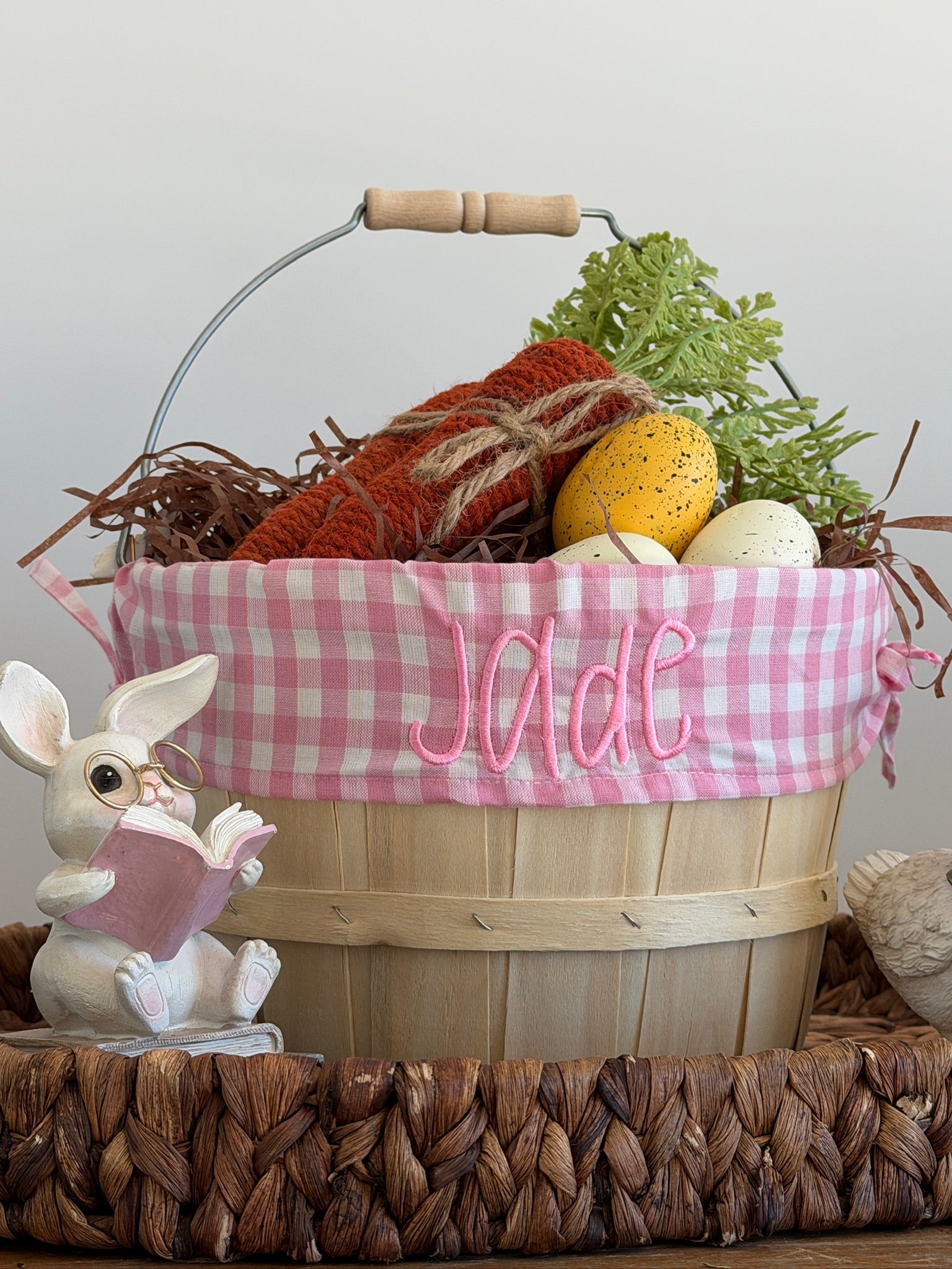 Decorative Easter basket with pink checkered liner, Easter eggs, and a bunny figurine on a wooden surface.