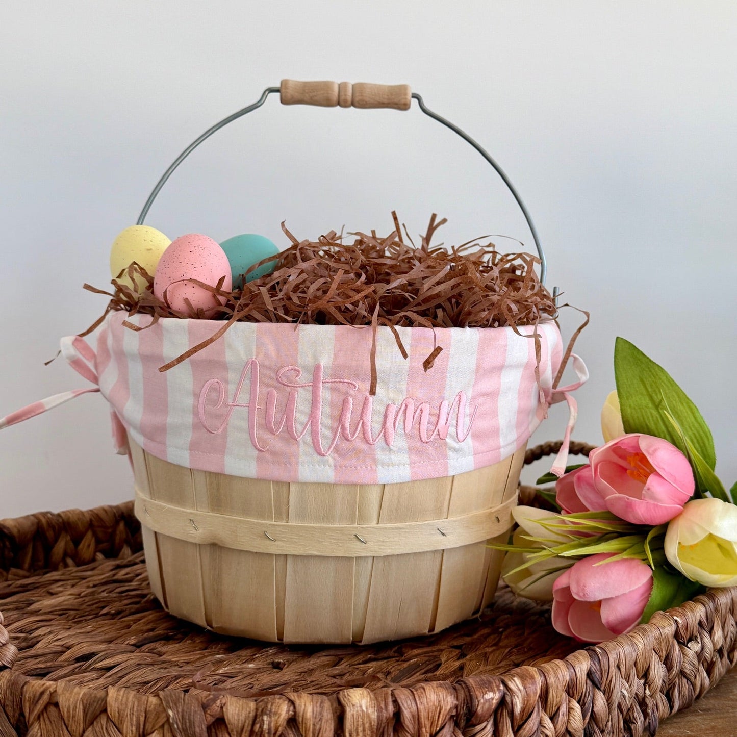 Decorative Easter basket with pink and white checkered lining, Easter eggs, and flowers on a wooden surface.