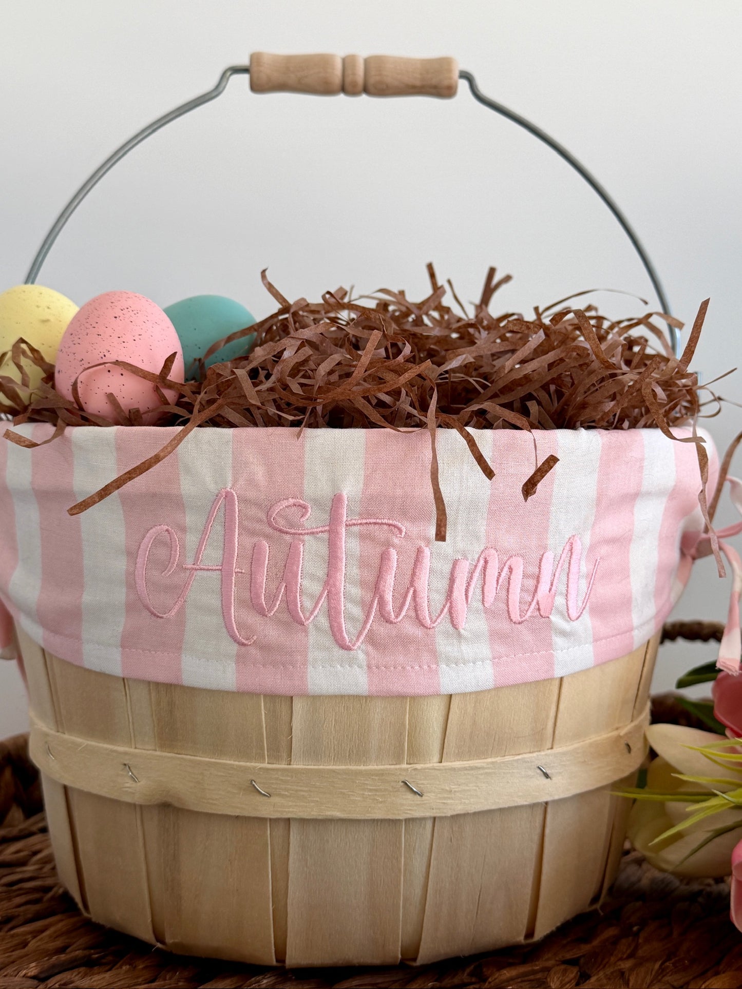 Wooden basket with pink and white striped lid labeled 'Autumn', filled with decorative eggs and hay.