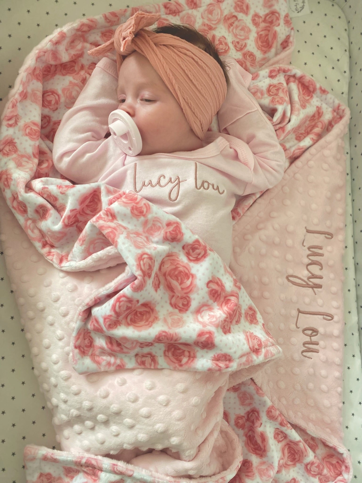 Newborn baby wrapped in a pink and white floral blanket with 'Lucy Lou' branding.