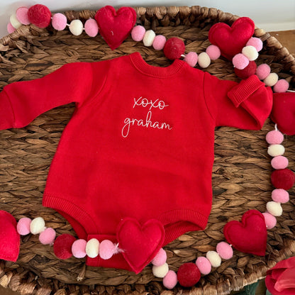 Red baby onesie with 'xoxo graham' text on a decorative mat with heart shapes.